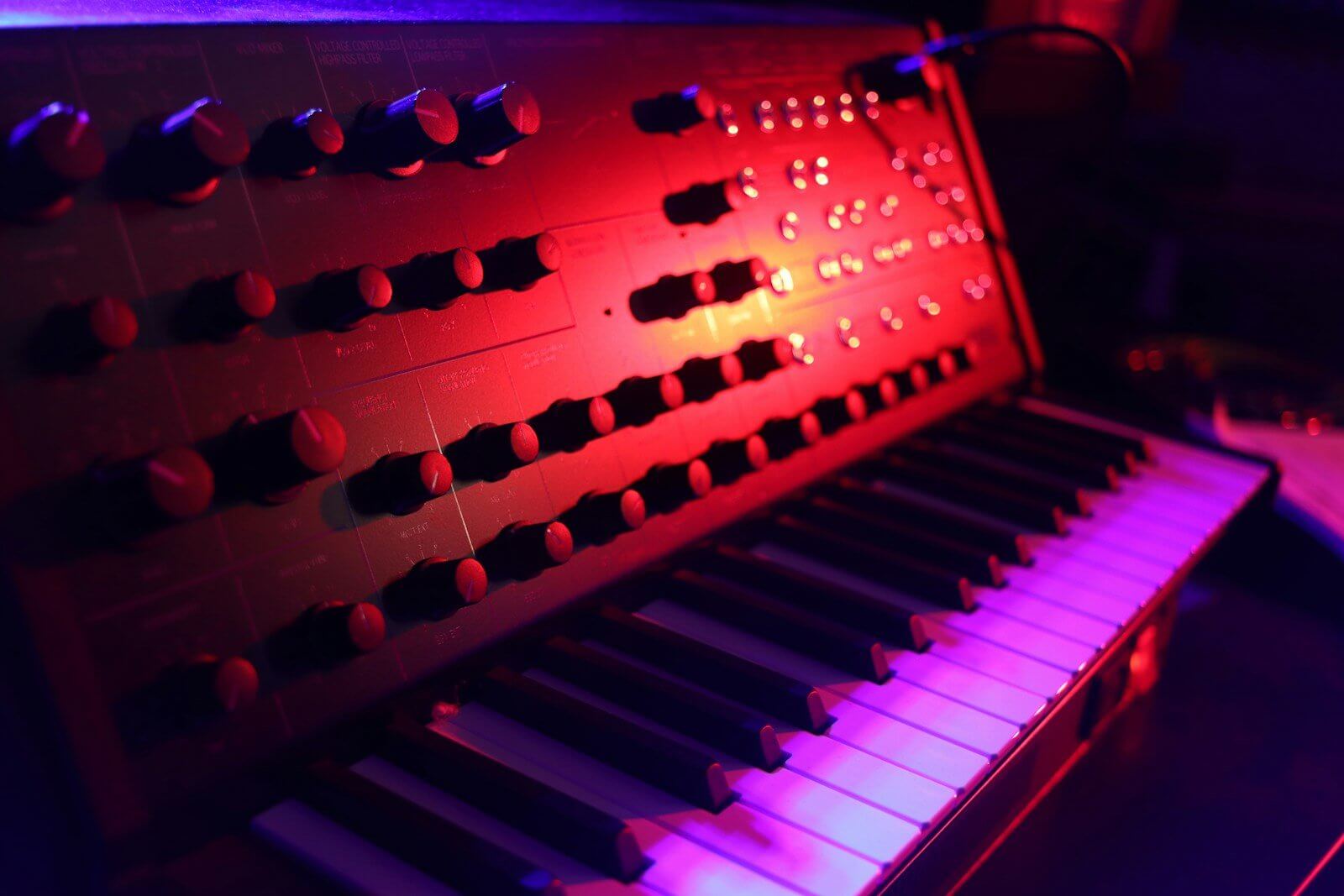 Analogue synthesizer with rows of knobs and a keyboard, lit red and purple